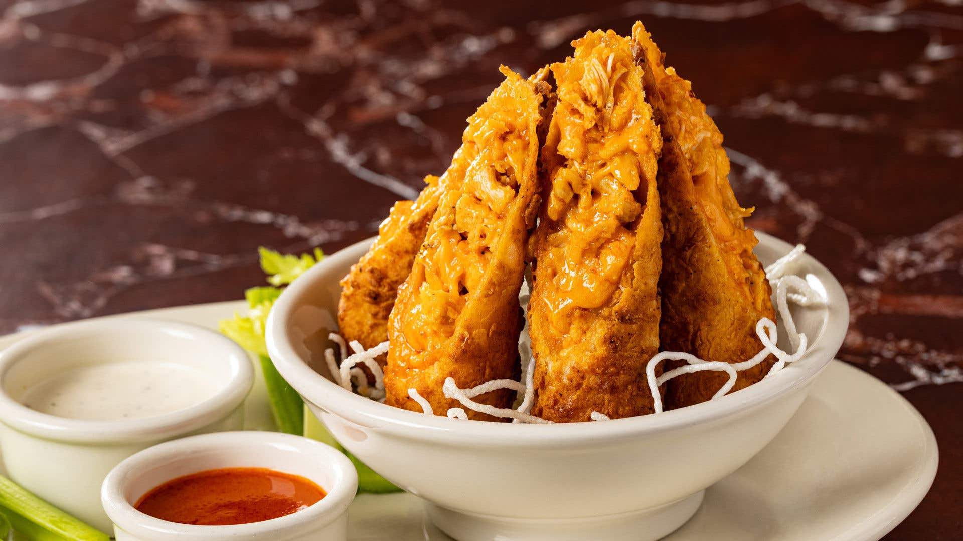A white plate with a variety of dipping sauces and buffalo chicken egg rolls arranged standing in a small bowl.