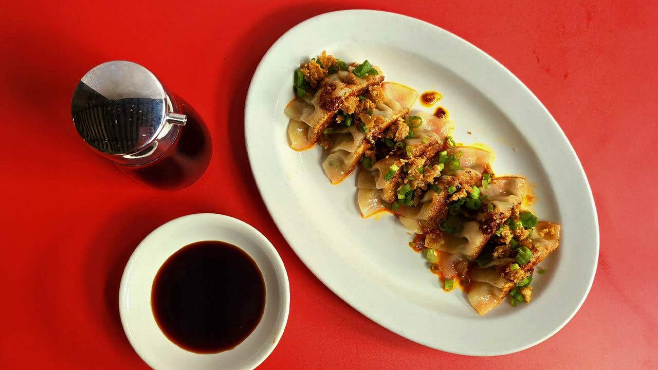 Gyoza topped with crispy chicken skin and sauce with soy sauce in a bowl and soy bottle on a table. 
