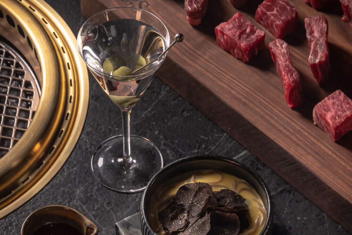 Martini glass with olives alongside sliced raw beef and a bowl topped with truffles.