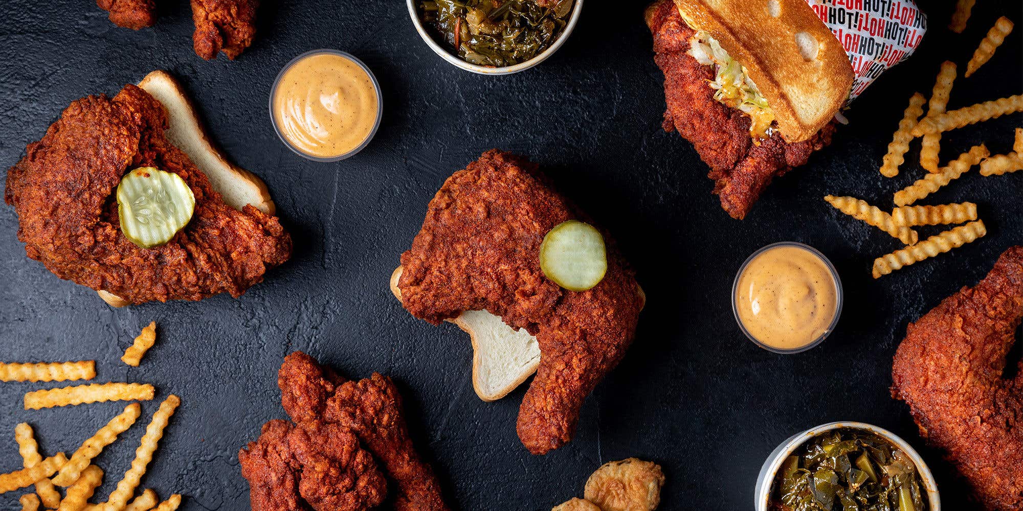 Fried chicken, sauce and collard greens displayed on a black table.  