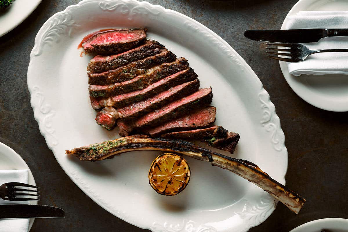 Steak sliced into pieces next to a large bone and a grilled half of lemon on a white plate.