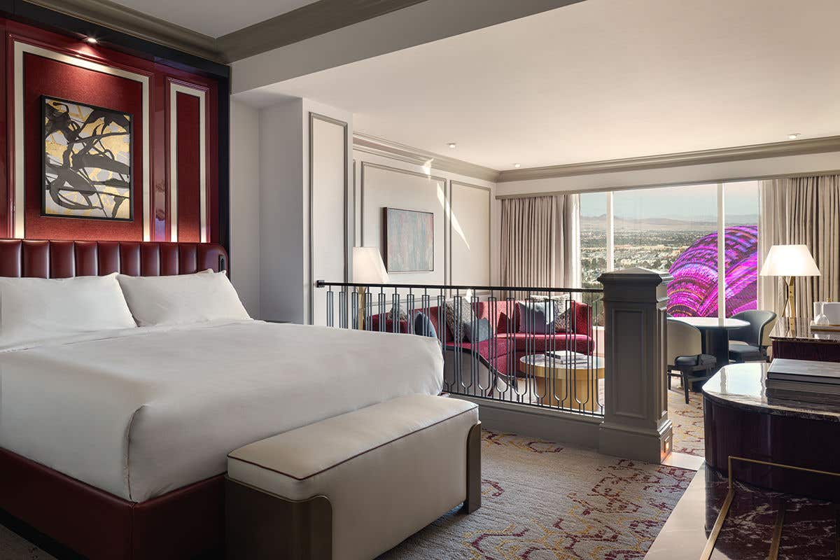 Newly Remodeled Luxury King Suite with a large bed, abstract artwork, and a sitting area with a sofa, overlooking Sphere at The Venetian in the window.