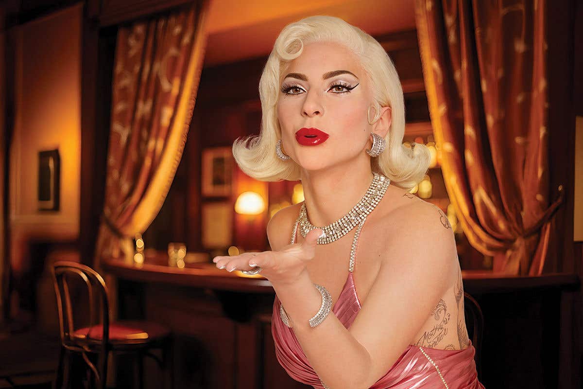 A wax figure of Lady Gaga with winged eyeliner in a pink dress and lots of diamonds, blowing a kiss.