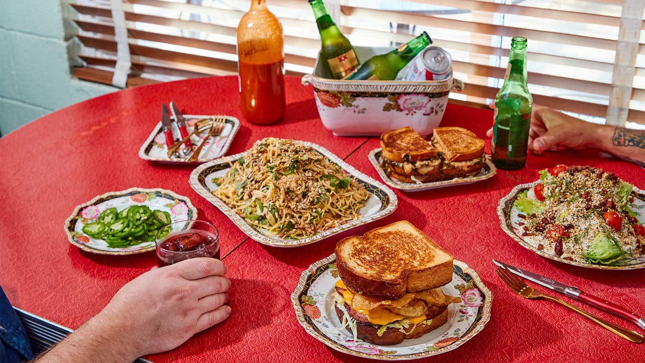 Red table with individual plated sandwiches, jalapeños, noodles and salad. 