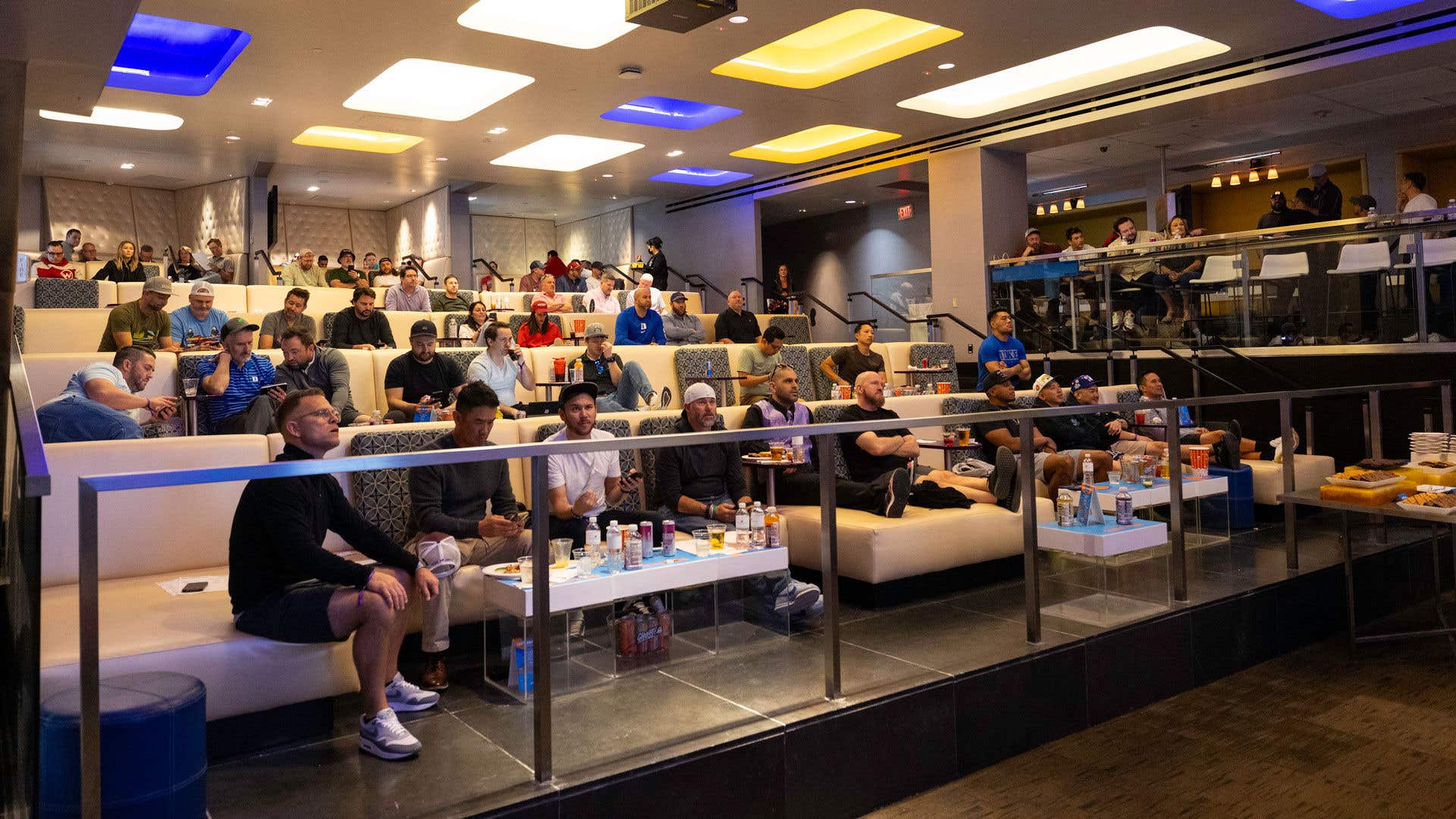 People sitting in seating area facing forward watching different screens.