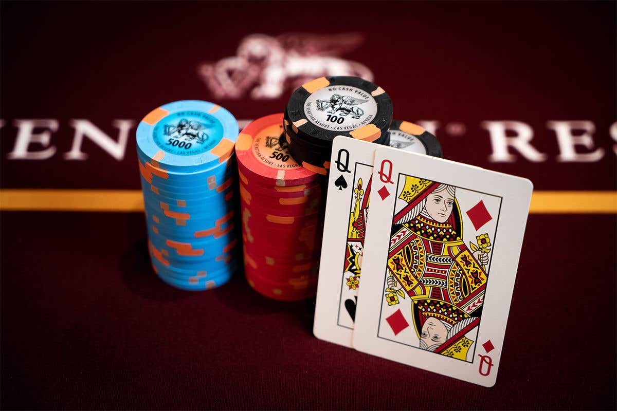 Poker chips and two Queens of playing cards on a maroon poker table.
