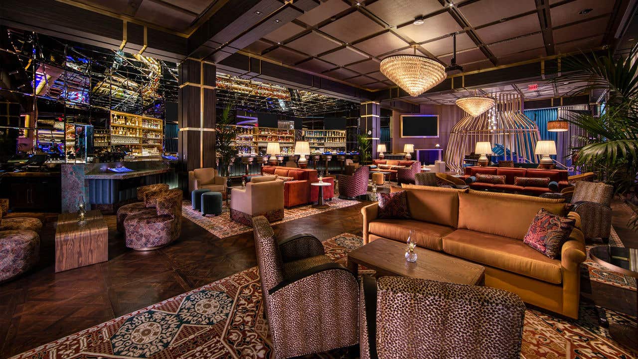 An eclectic bar with vibrant patterned velvet couches and ottomans, intricate carpets and a deep wood floor.