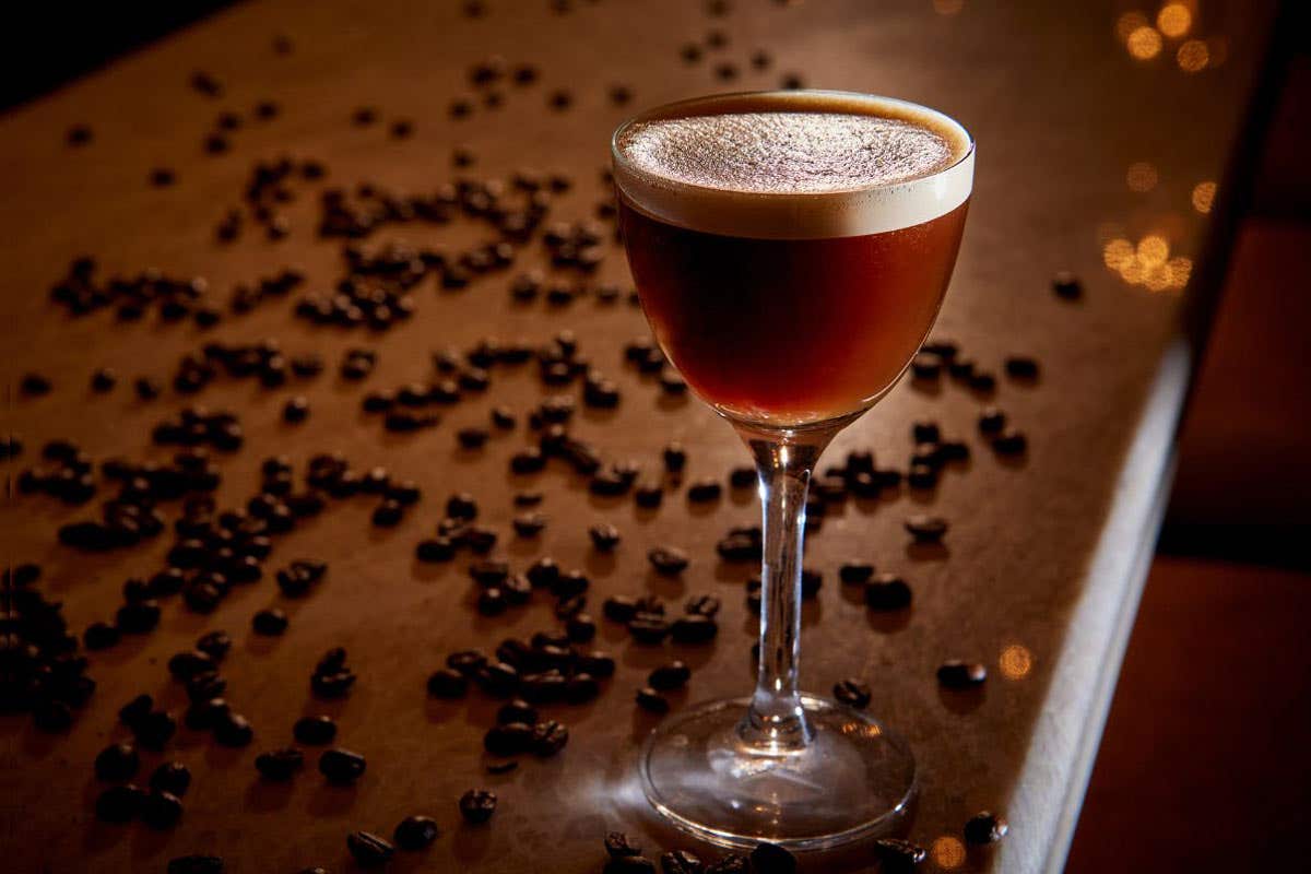 Espresso martini on a bar surrounded by coffee beans.
