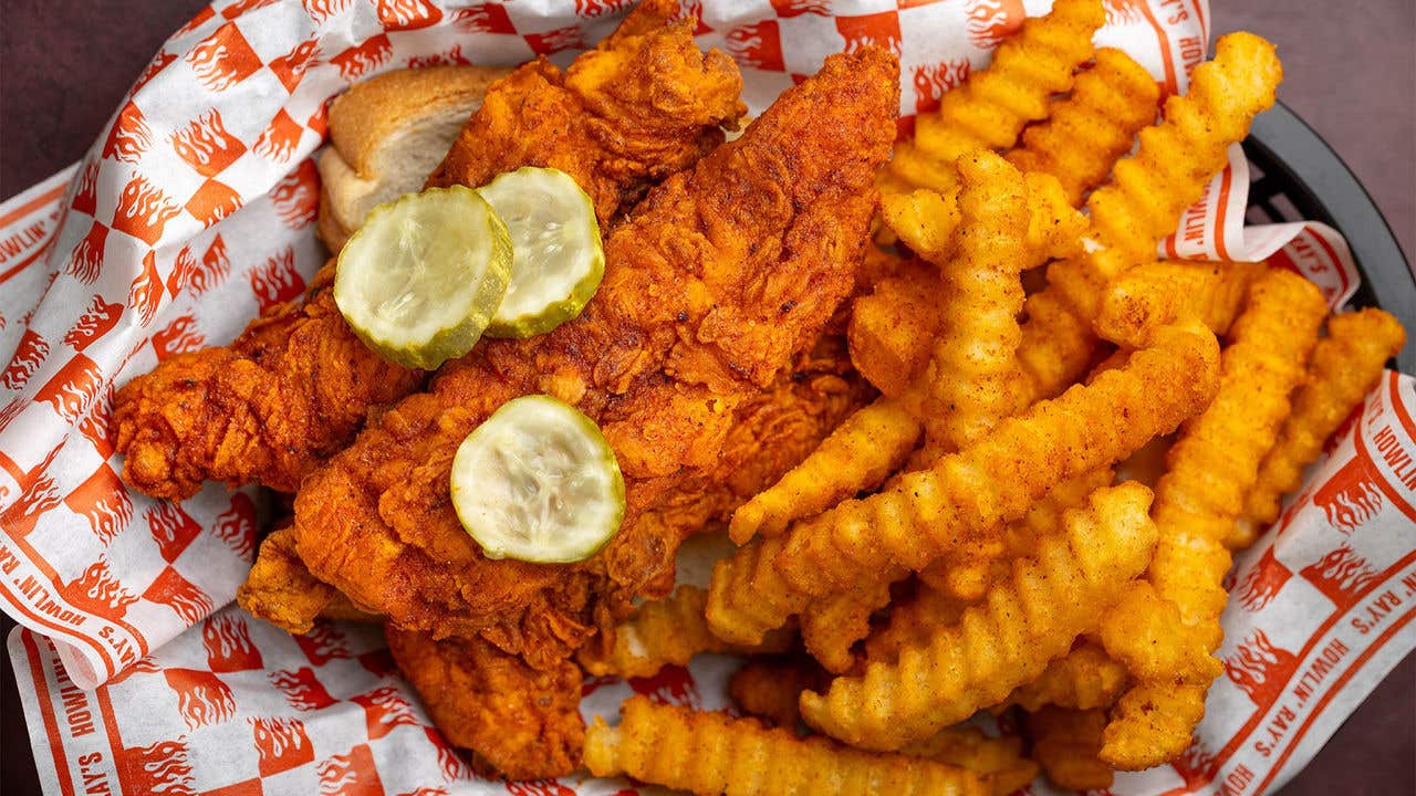 Fried chicken with sliced pickles on top with crinkle fries on graphic paper. 