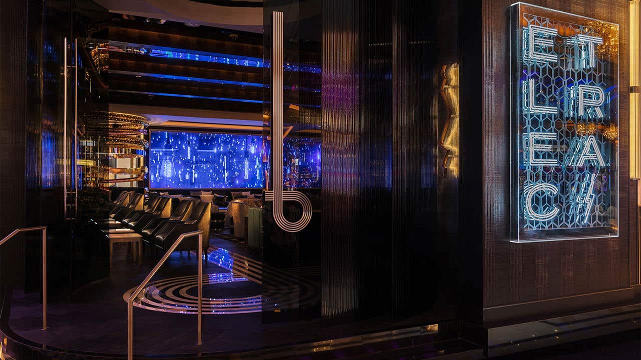 Steps leading into a dimly lit bar. Neon signs spells Electra and a large video screen is visible beyond the entrance.