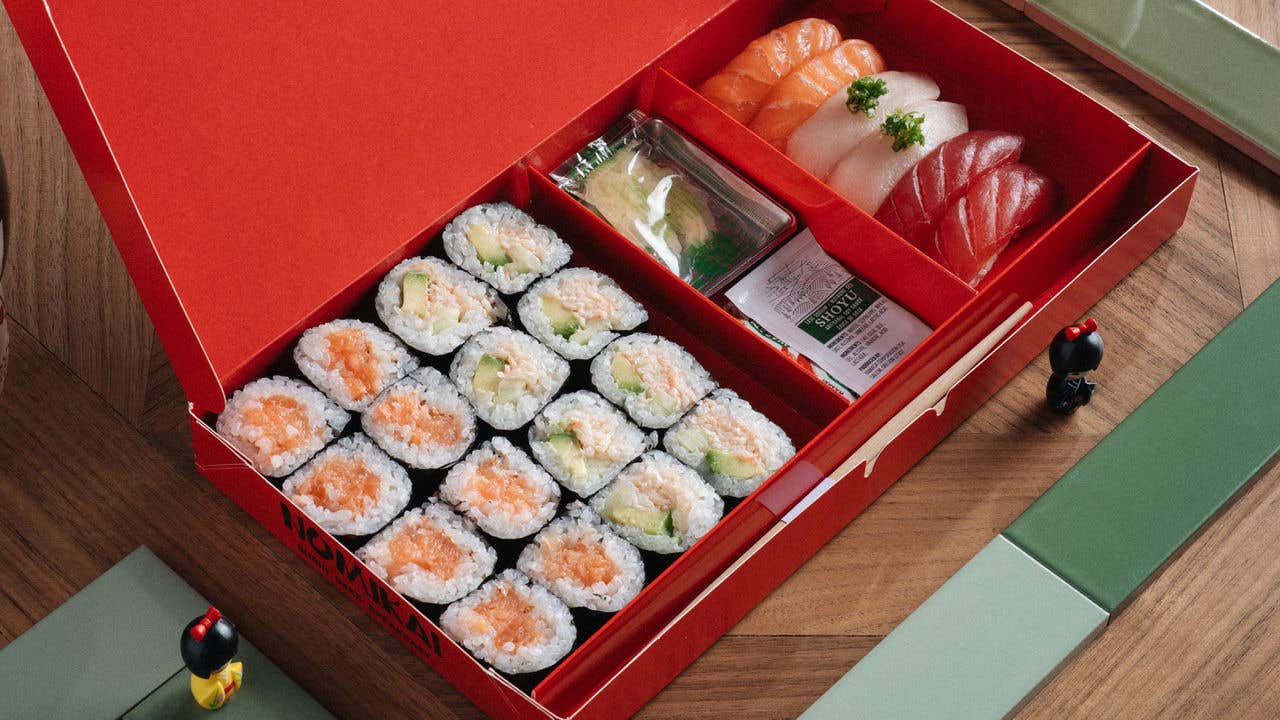 Red bento box with assorted sushi, including maki rolls and sashimi, on a wooden table.