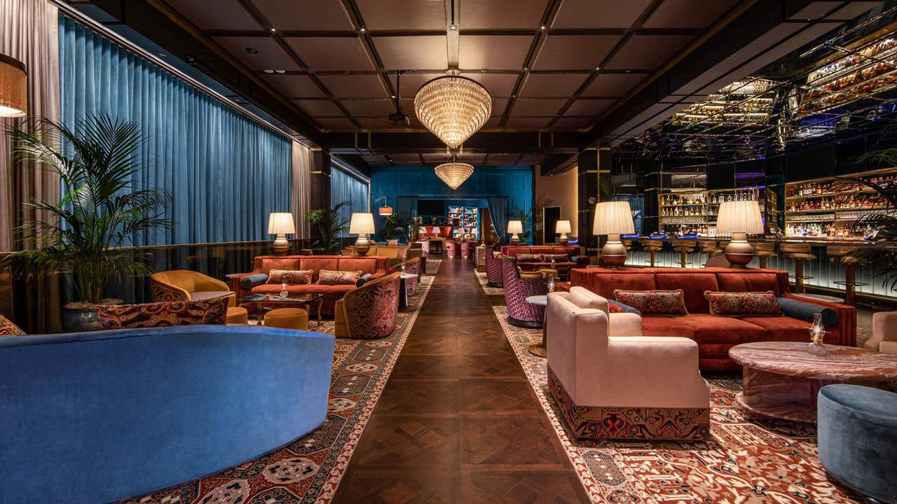 A long view of the lounge with blue curtains, red couches and a teal wall leading into a library.