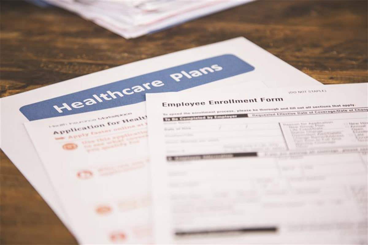 A close-up of healthcare plan documents and an employee enrollment form spread out on a wooden desk